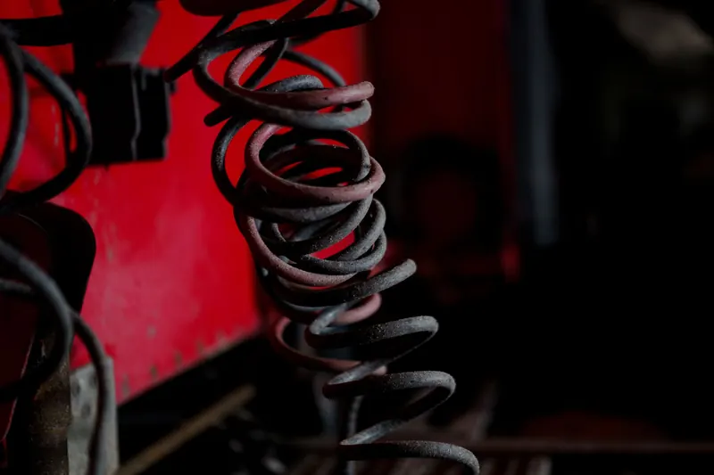 Close-up of old, worn metal coil springs against a red painted surface
