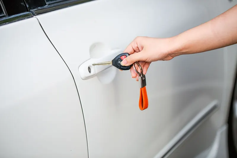 A hand turning a remote-head key in the door lock of a white car