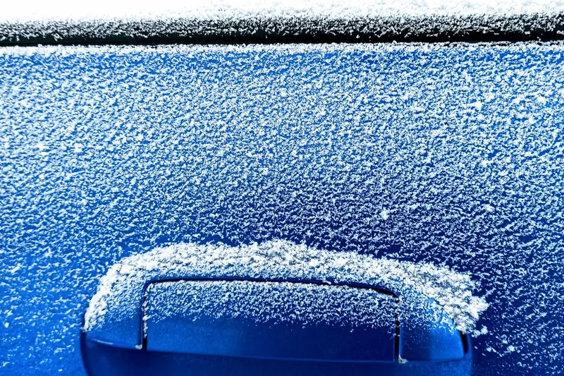 Close-up of a car door handle and panel covered in white frost crystals