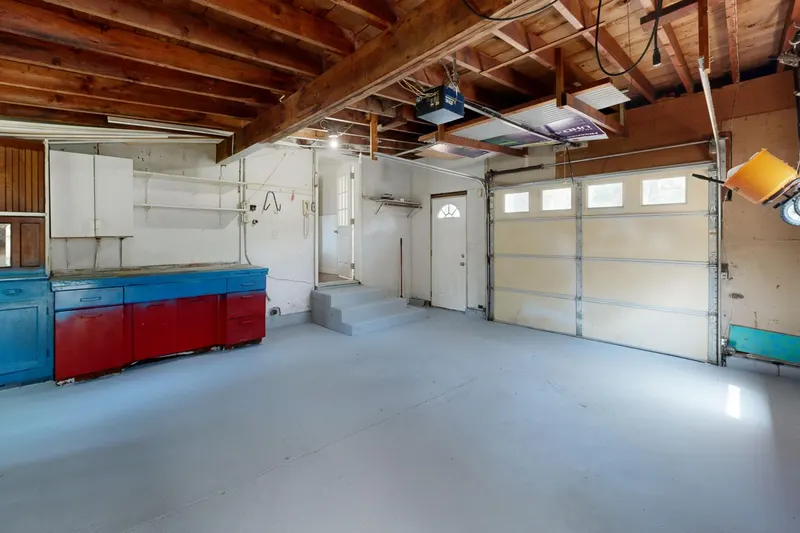 A closed white sectional garage door inside an empty garage, below a ceiling-mounted opener and rail