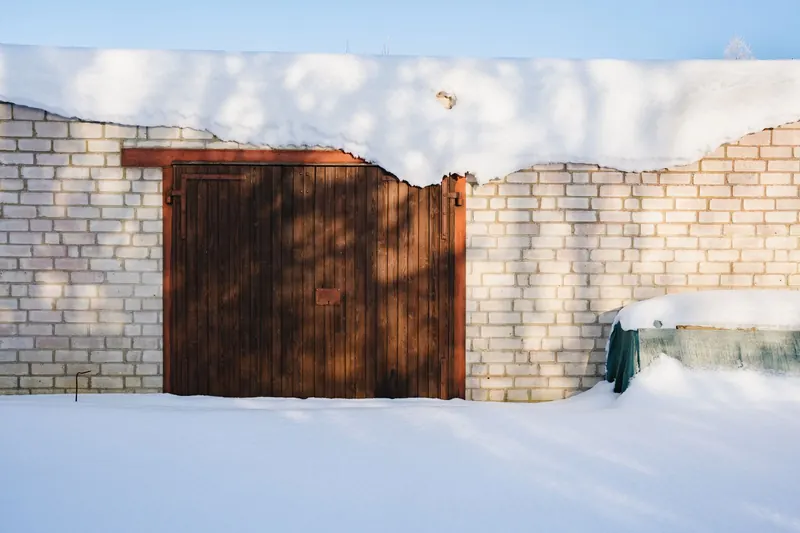 A wooden garage door set in a white brick wall, with snow drifted against its base