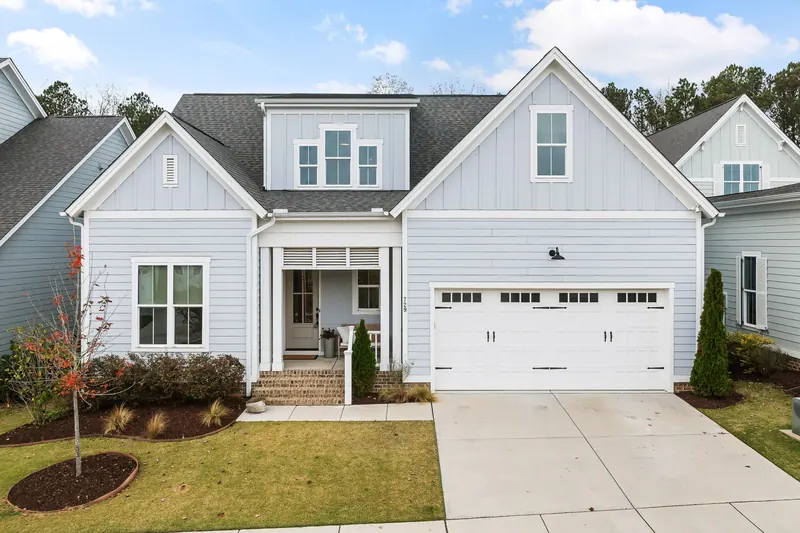 A pale blue two-storey house with a white double garage door and a concrete driveway