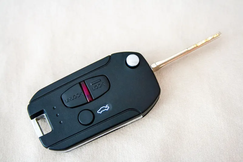 A black flip-style car key fob with lock, unlock and trunk buttons, its metal blade folded out