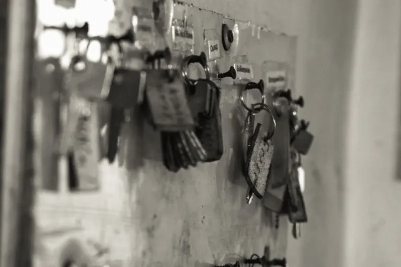 Black and white photo of sets of keys with handwritten tags hanging on hooks on a key board