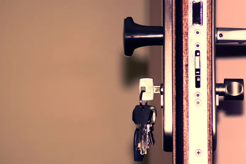 The edge of an open door showing the lock body and bolt, with a bunch of keys hanging from the cylinder
