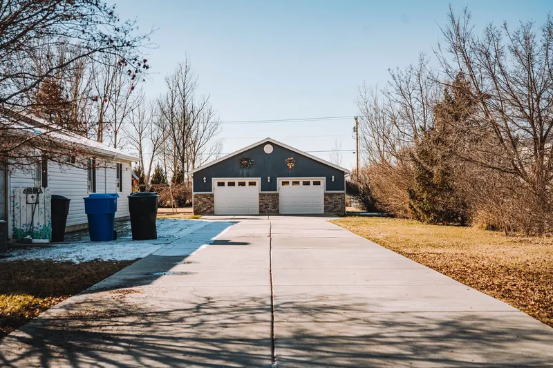 A long driveway with patches of snow leading to a detached double garage with two white doors