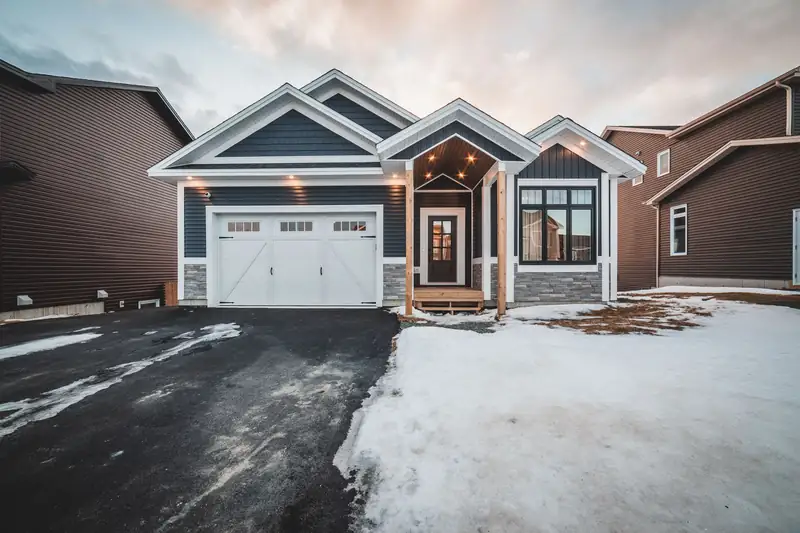 A house with a white garage door and porch lights on a snowy evening