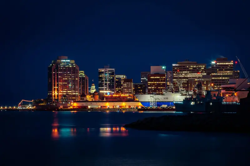 Downtown Halifax lit up at night across the harbour, with ships at the dockyard and lights reflected in the water