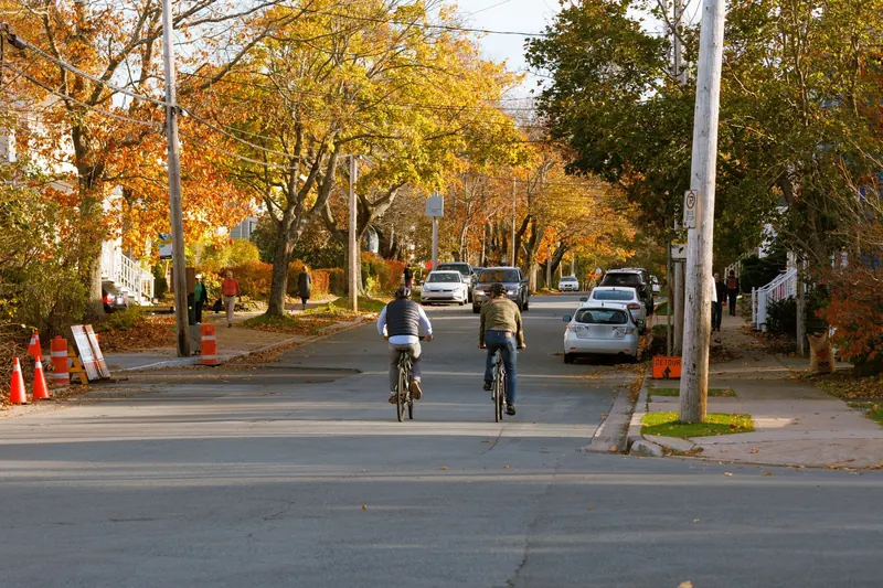 A tree-lined Halifax street in autumn, wooden houses behind the maples and two cyclists riding away