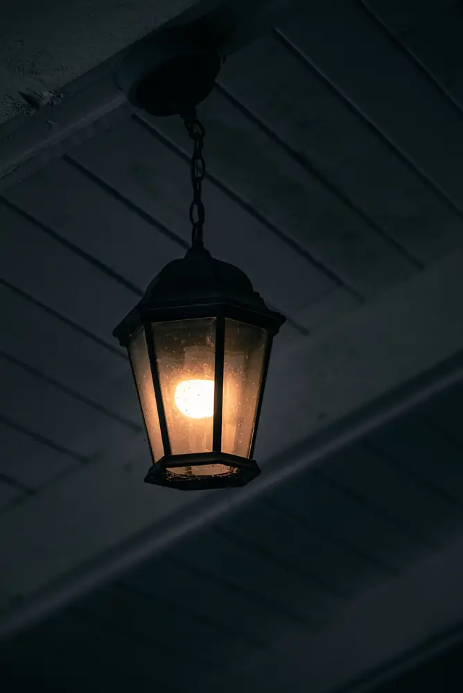 A single lit lantern under a dark porch roof
