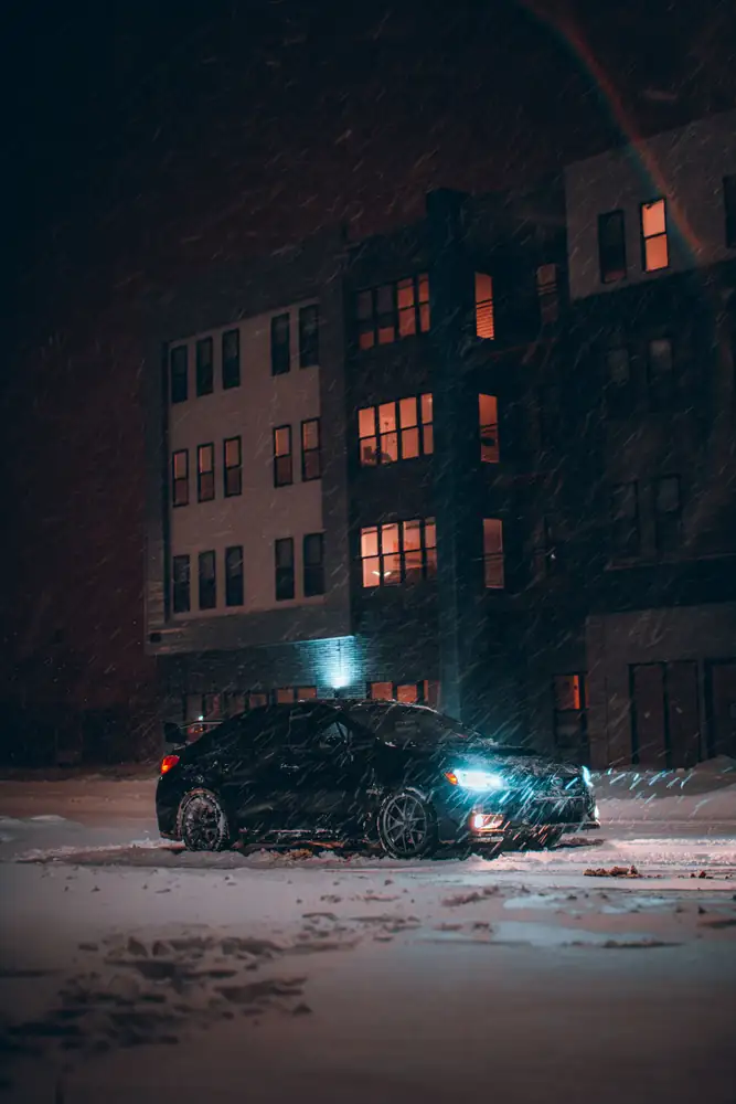 A car with headlights on in a snowy lot at night